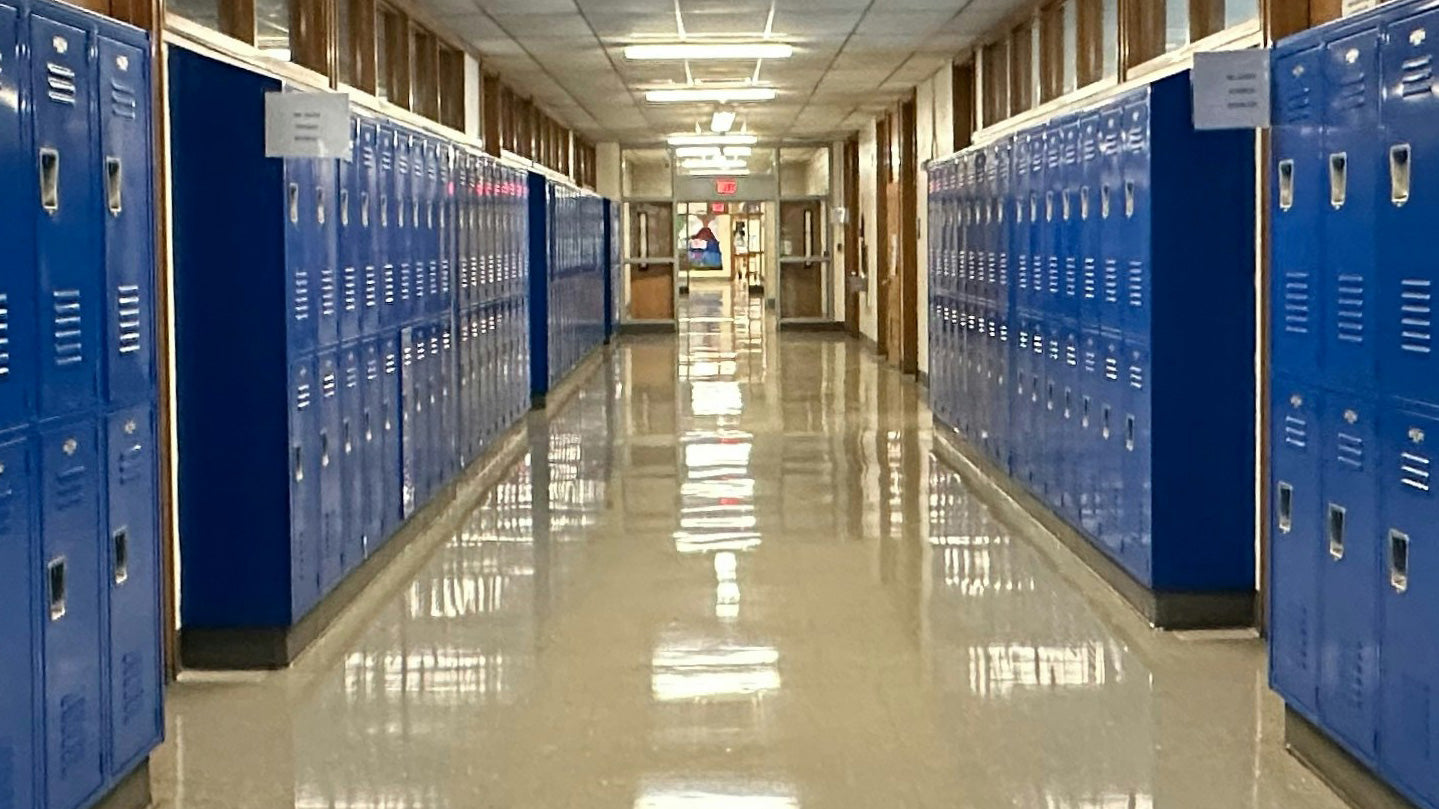 A long, brighly lit school hallway with bright blue lockers on either side.