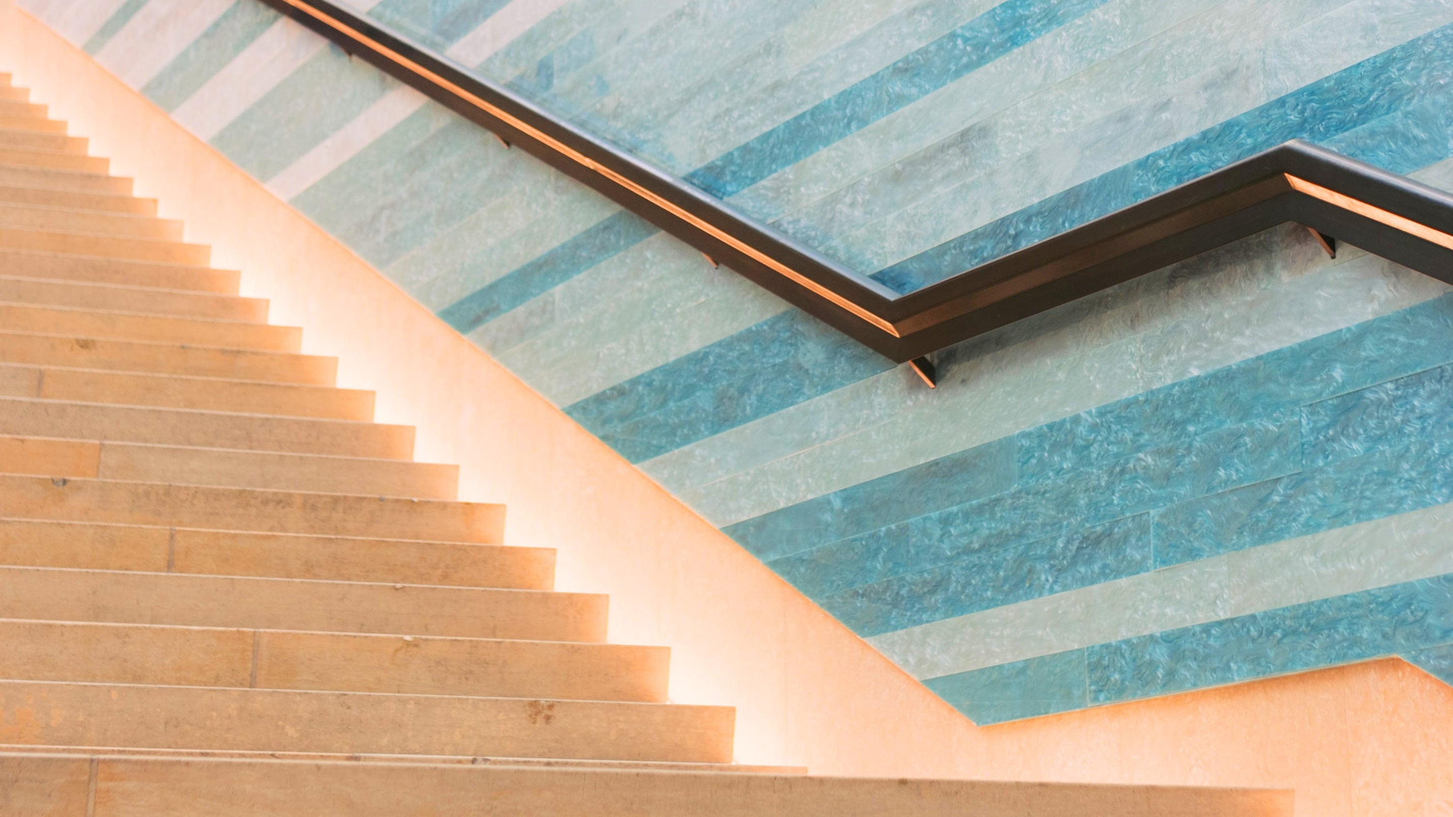 A side-view of a warm stone staircase and bronze handrail strongly suggesting upward movement.